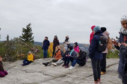 Ryhmä henkilöitä istuu tai seisoo kalliolla, taustalla syksyinen vaaramaisema.