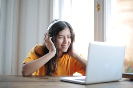 Tyttö istuu pöydän ääressä tietokoneen ääressä, päässä kuulokkeet