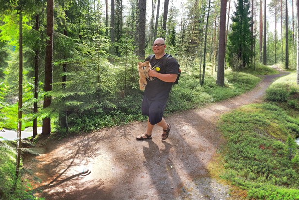 Mies kävelee metsässä pieni koira sylissään