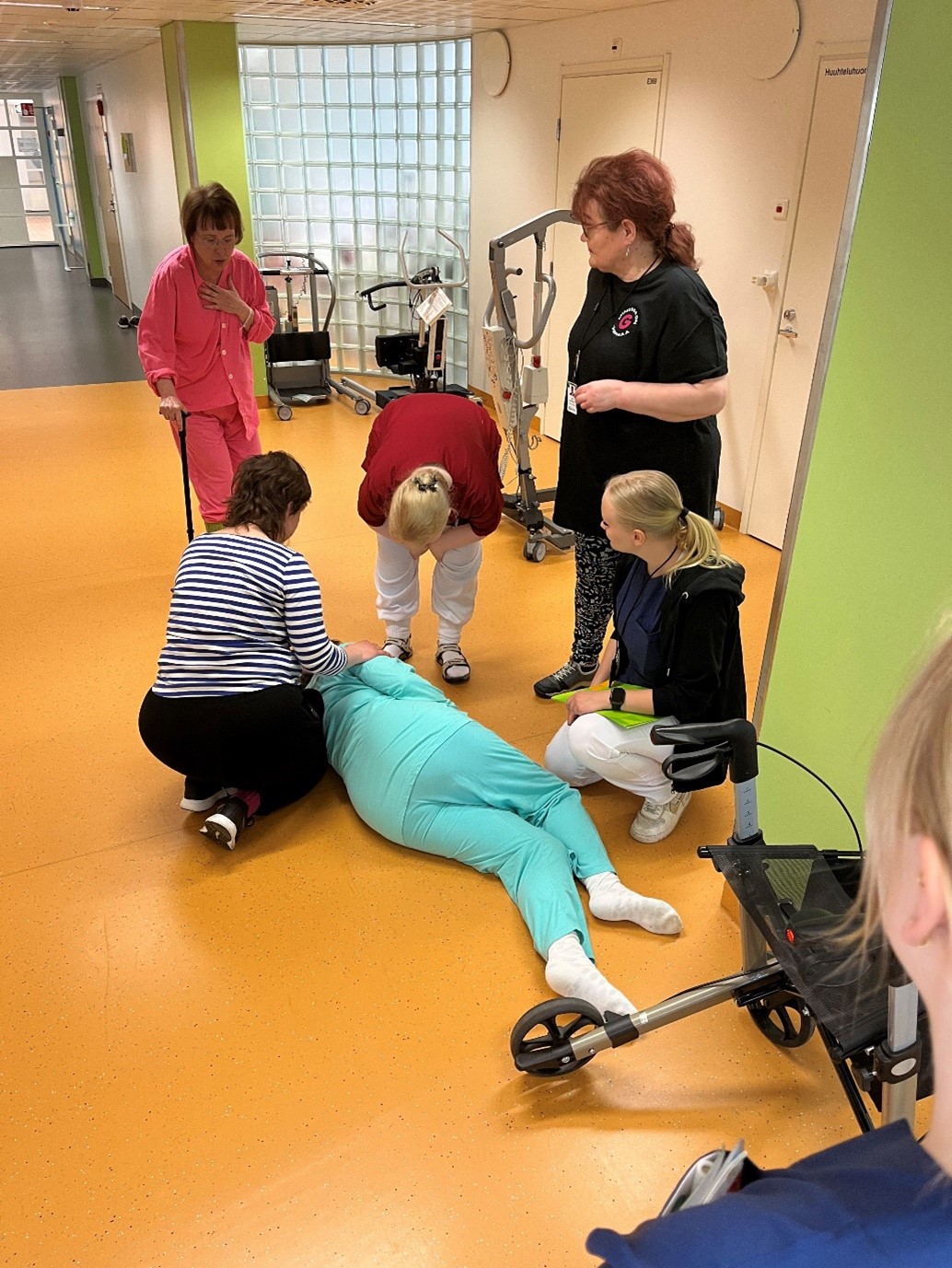 Potilas makaa lattialla, ympärillä henkilöitä auttamassa
