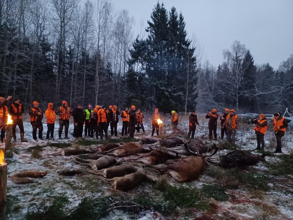 Henkilöitä pukeutuneina metsästysasuun. Keksellä metsästyksessä kaadettuja eläimiä